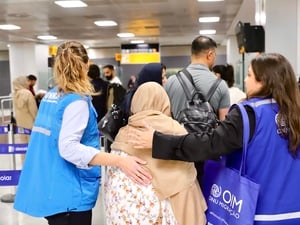 Staff from UNHCR and IOM walk through a crowded airport with their arms around a woman