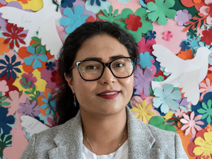 A woman stands in front of a wall decorated with flowers.