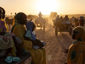The sun lights up the dust behind groups of Sudanese refugees walking and on carts behind horses